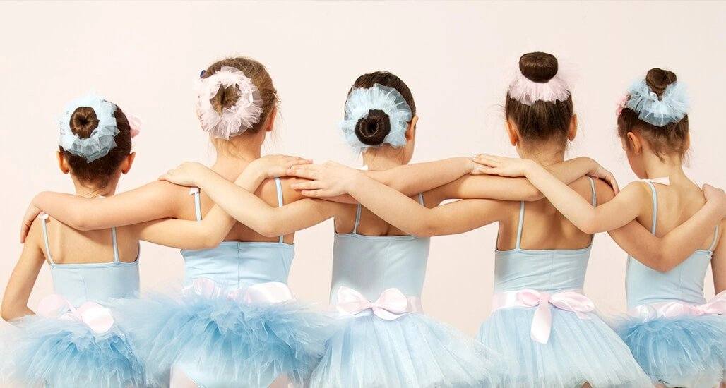 A row of young ballet students standing with arms linked