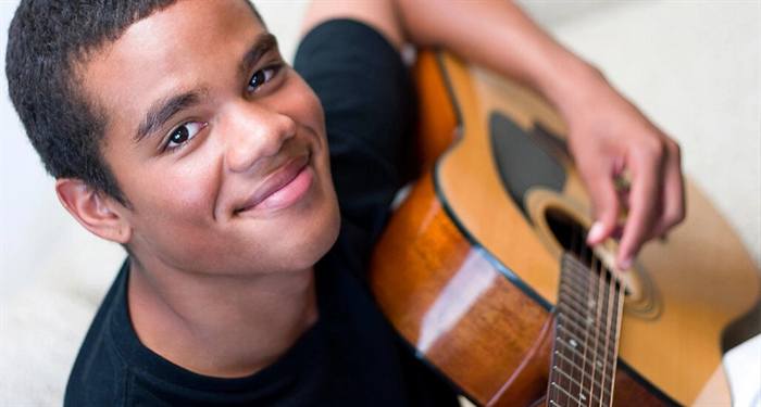 Student smiling while playing an acoustic guitar